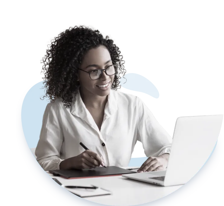 A woman with curly hair and glasses is smiling as she works on a laptop. She is wearing a white shirt and appears to be engaged in her work. She is studying project management with Link Education.